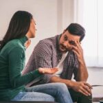 Pareja sentada en el sofá en plena conversación seria, ejemplificando los desafíos emocionales de cómo hablar con tu pareja sobre el VIH con empatía.