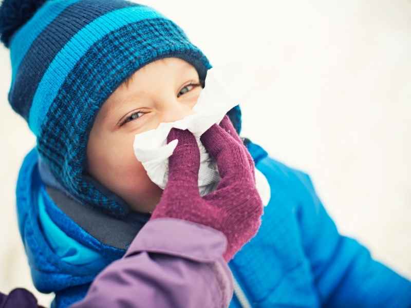 Niño abrigado en invierno mientras un adulto le limpia la nariz, ilustrando síntomas respiratorios comunes en temporada fría.