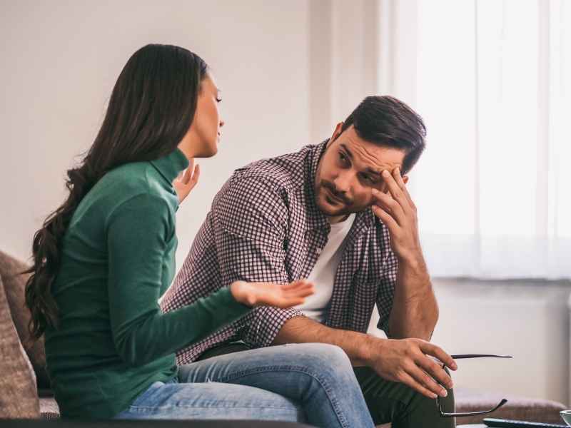 Pareja sentada en el sofá en plena conversación seria, ejemplificando los desafíos emocionales de cómo hablar con tu pareja sobre el VIH con empatía.
