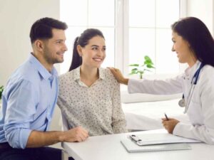 Pareja sonriente conversando con una doctora, representando un momento de acompañamiento luego de decidir cómo hablar con tu pareja sobre el VIH.